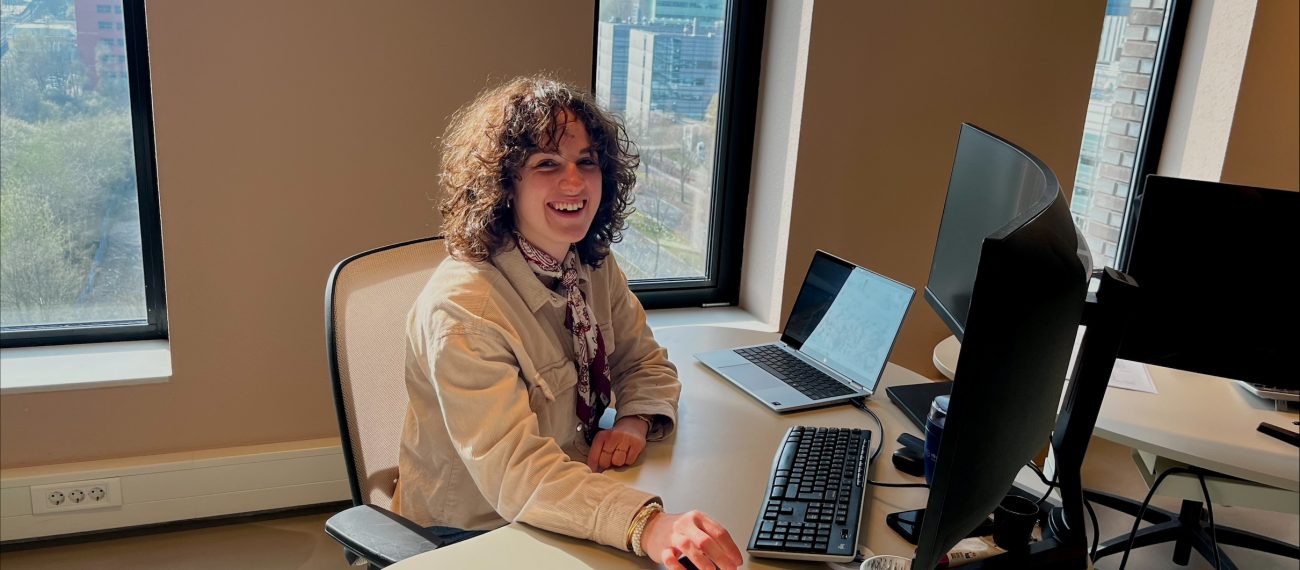 Medewerker zit aan bureau met laptop en monitor in modern kantoor met grote ramen en uitzicht op stad, werkt geconcentreerd