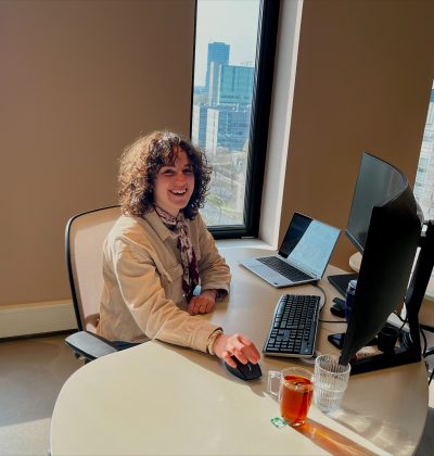 Medewerker zit aan bureau met laptop en monitor in modern kantoor met grote ramen en uitzicht op stad, werkt geconcentreerd