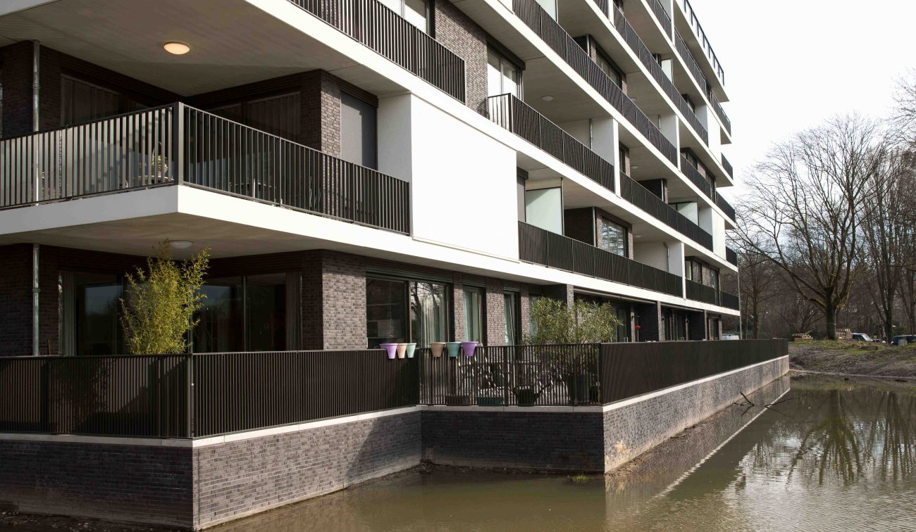 Moderne woonblokken met witte horizontale banden, donkere baksteen en terrassen aan het water — Ontwikkeling Het Schrijverskwartier Eindhoven