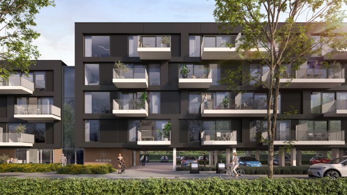 Close-up van Maison L’Europe in Helmond: modern donker appartementencomplex met uitstekende witte balkons en grote ramen, op kolommen met doorgang naar de parkeergarage; bomen, een fietser en voetgangers op de voorgrond.