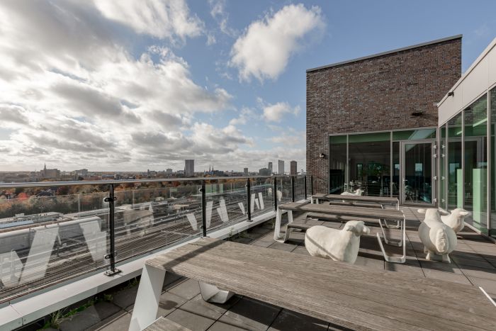 Dakterras met picknickbanken en glazen balustrade, uitzicht over skyline Eindhoven — Ontwikkeling Dorgelo Building Eindhoven