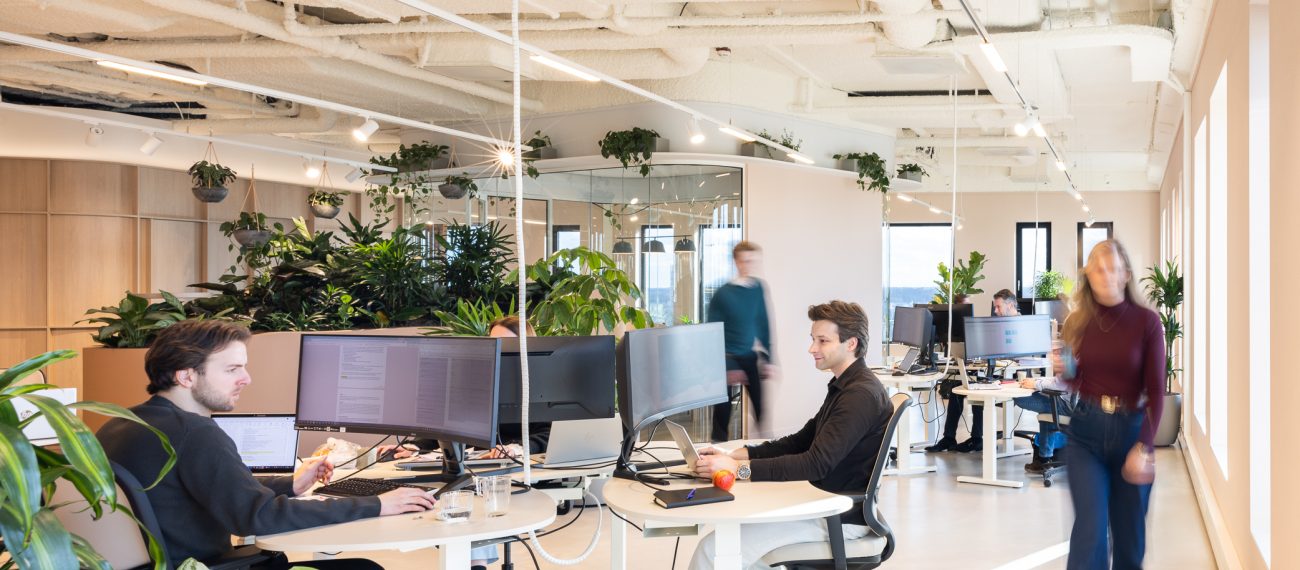 Moderne kantoorruimte met veel planten waar medewerkers werken aan bureaus in een licht en open interieur.