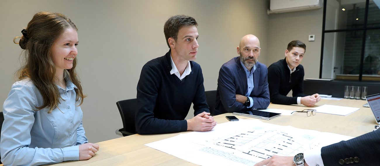 Groep mensen in vergaderruimte bespreekt bouwtekeningen aan tafel