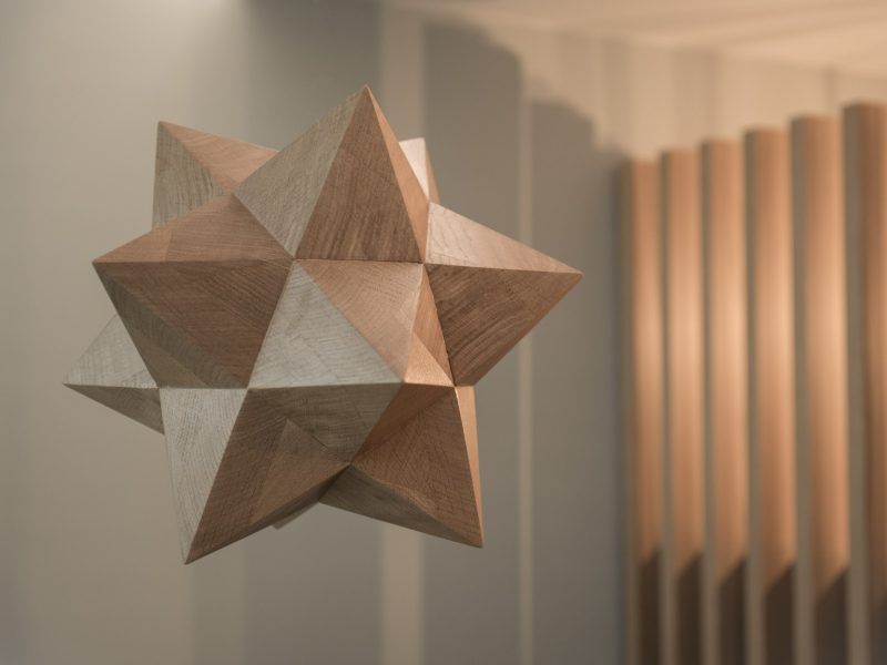 Abstract houten kunstobject met geometrische vormen, tentoongesteld in modern interieur met warme verlichting.