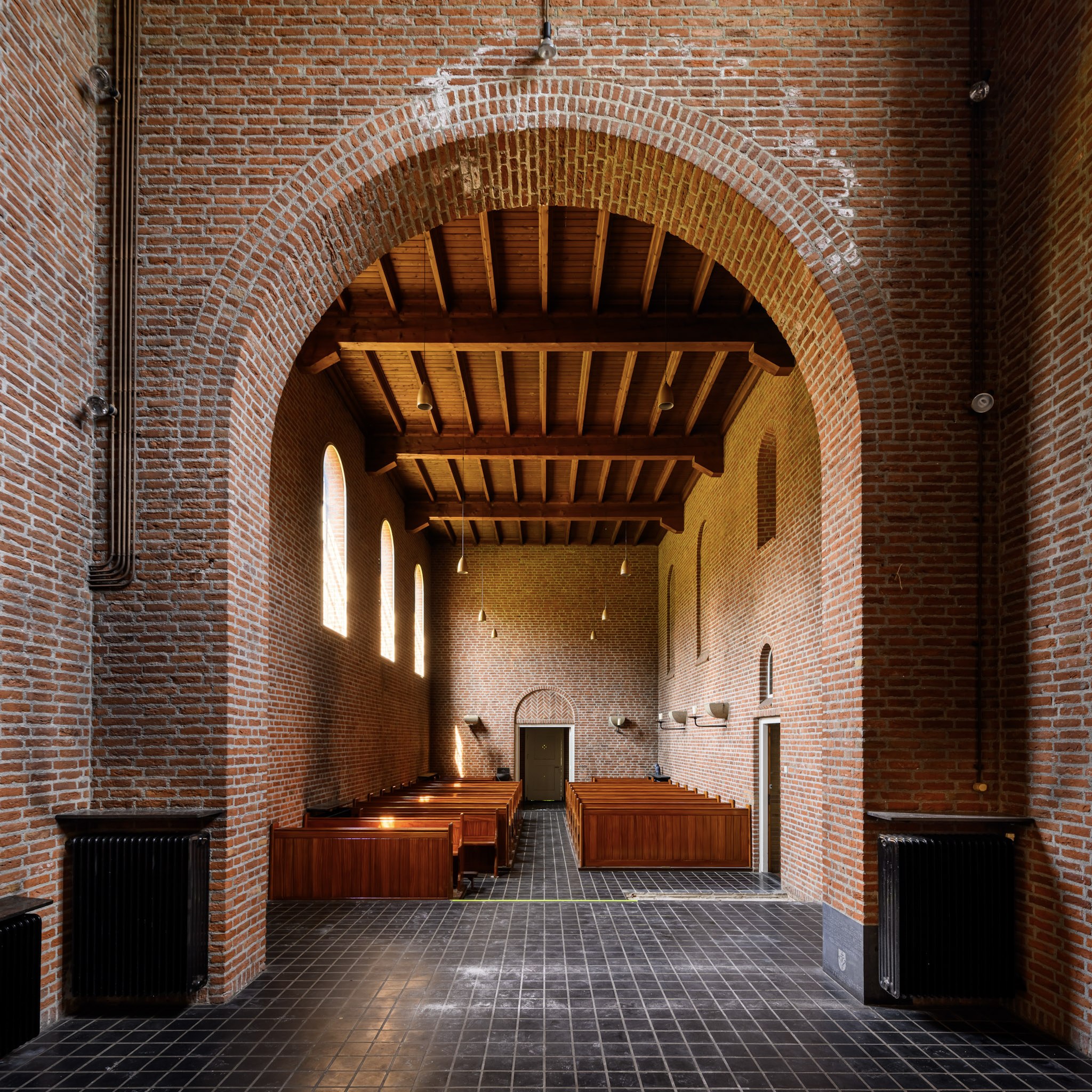 Kerkinterieur met bakstenen bogen, houten plafond en rijen kerkbanken