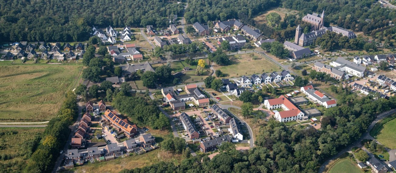 Kloostervelden Sterksel – luchtfoto van woonwijk rond kloostercomplex met kerktorens, rijwoningen en vrijstaande huizen aan de bosrand