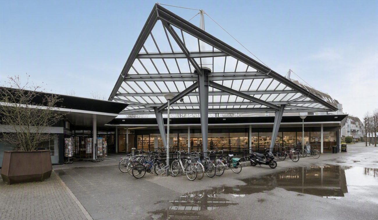 Fietsenstalling met stalen driehoekige dakconstructie en glazen overkapping bij gebouwentree