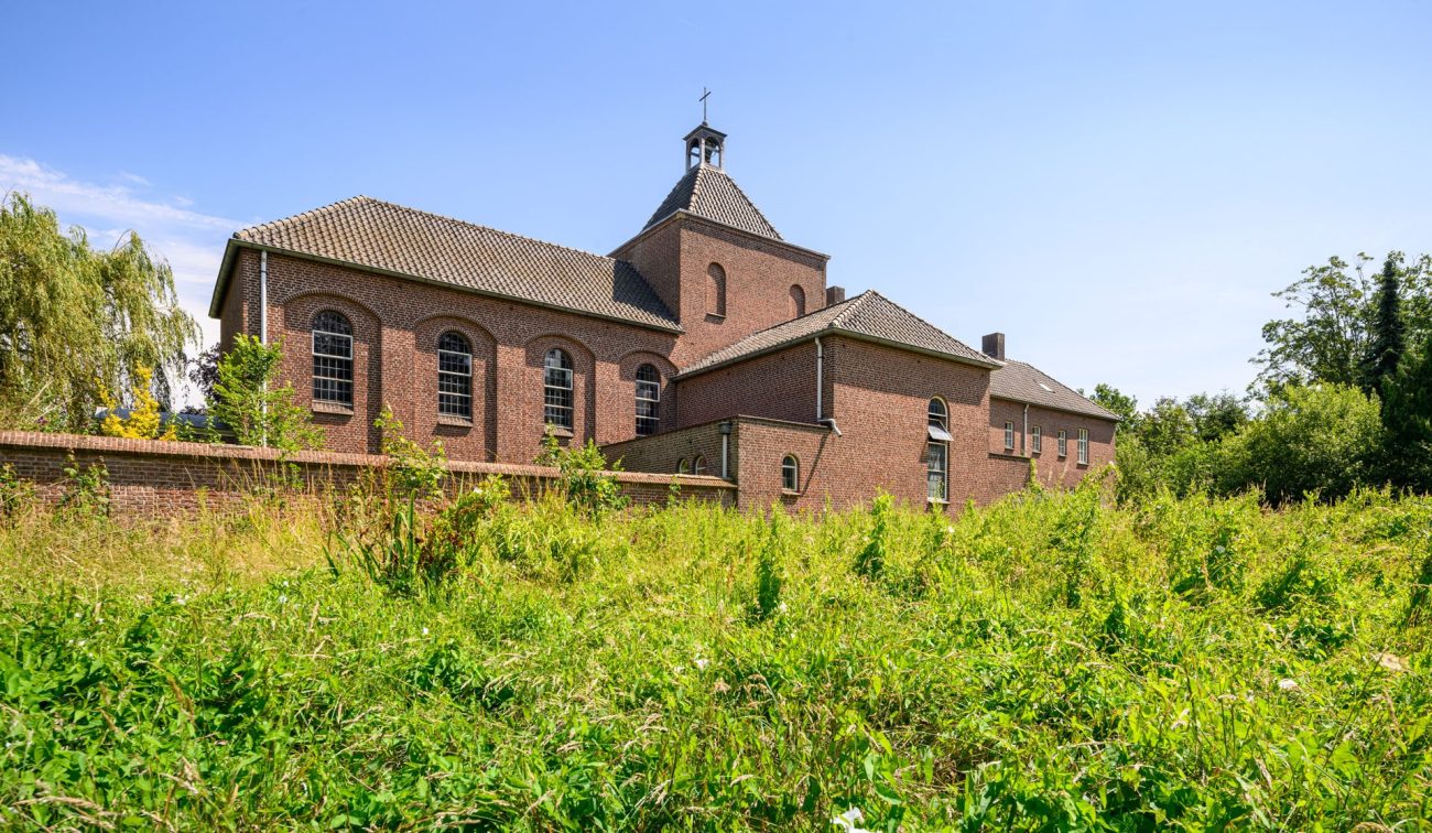 Historisch kloostergebouw in Eindhoven met rondboogvensters, gezien vanaf weide — Transformatie Clarissenklooster Eindhoven