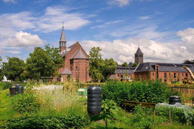 Klooster en nieuwbouwwoningen in Kloostervelden in Sterksel met zonnepanelen op de daken en een groene moestuin op de voorgrond.