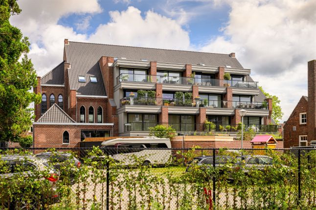 Zijaanzicht van De Antonius in Valkenswaard waarop de balkons en de aangrenzende parkeerplekken zichtbaar zijn tijdens de transformatie van het gebouw.