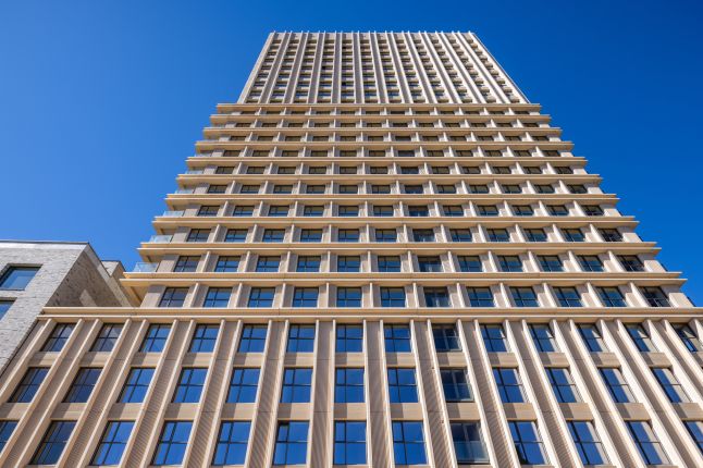 Ontwikkeling De Bankier Tilburg – close-up omhoogkijkend perspectief van de toren met ritmische geveldetaillering en grote raamvlakken tegen een helderblauwe lucht.