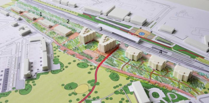 Planmaquette van parkstrook met woningen, rode hoofdroute en stationsomgeving op de achtergrond