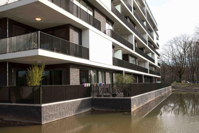 Begane-grond terrassen met hekwerk langs water en bovenliggende balkonlagen — Ontwikkeling Het Schrijverskwartier Eindhoven