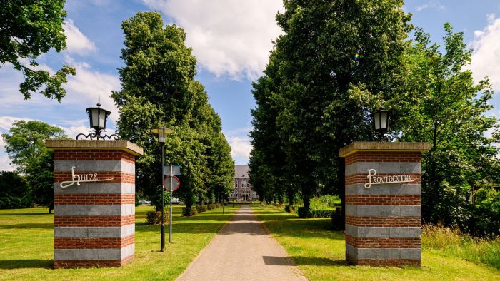 Toegangslaan met bakstenen zuilen ‘Huize’ en ‘Providentia’, bomenrij en monumentaal gebouw op de achtergrond