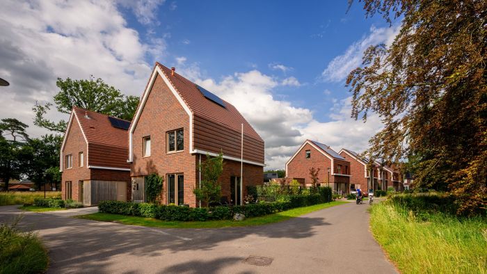 Nieuwbouwwoningen in Kloostervelden in Sterksel met rode baksteen, zonnepanelen en een groene straat met bewoners op de fiets.
