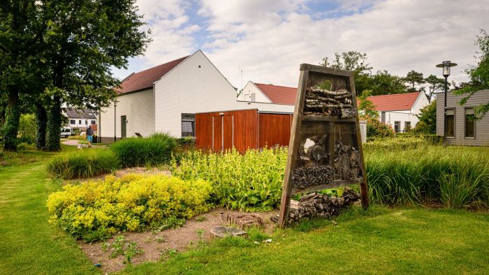 Natuurinclusieve woonwijk met insectenhotel, siergrassen en witte huizen met rode dakpannen