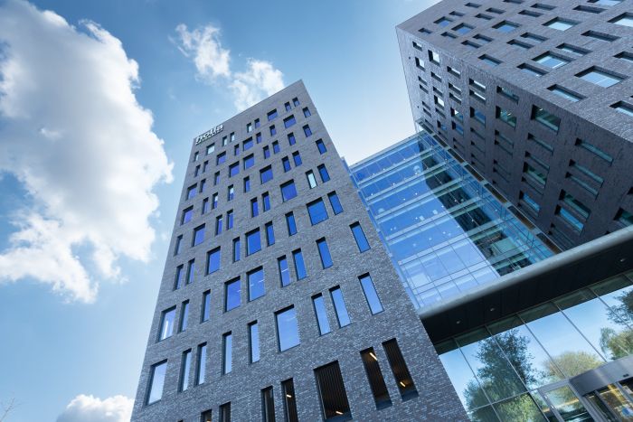 Grijze baksteentorens met glazen atrium en slanke raamstroken, tegen blauwe lucht — Ontwikkeling Dorgelo Building Eindhoven