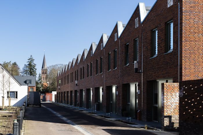 Rijwoningen met bakstenen gevels en hoge daklijnen langs smalle woonstraat in nieuwbouwwijk