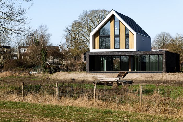 Vrijstaande nieuwbouwwoning met hoge raampartijen en donkere gevel aan groen landschap