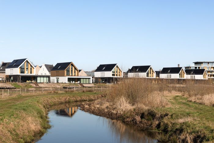 Nieuwbouwwoningen langs watergang met rietoevers in groene woonomgeving