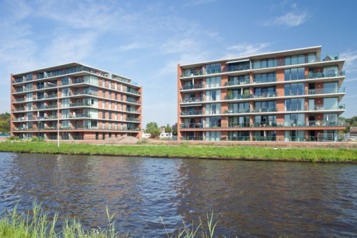 Twee wooncomplexen aan kanaal met balkons en baksteen-glas gevels — Ontwikkeling HIVA Son