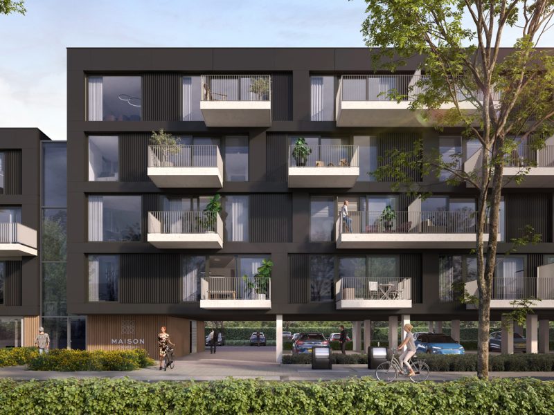 Close-up van Maison L’Europe in Helmond: modern donker appartementencomplex met uitstekende witte balkons en grote ramen, op kolommen met doorgang naar de parkeergarage; bomen, een fietser en voetgangers op de voorgrond.